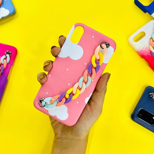 Pink phone case with white clouds and colorful chain charm, held in hand, on yellow background