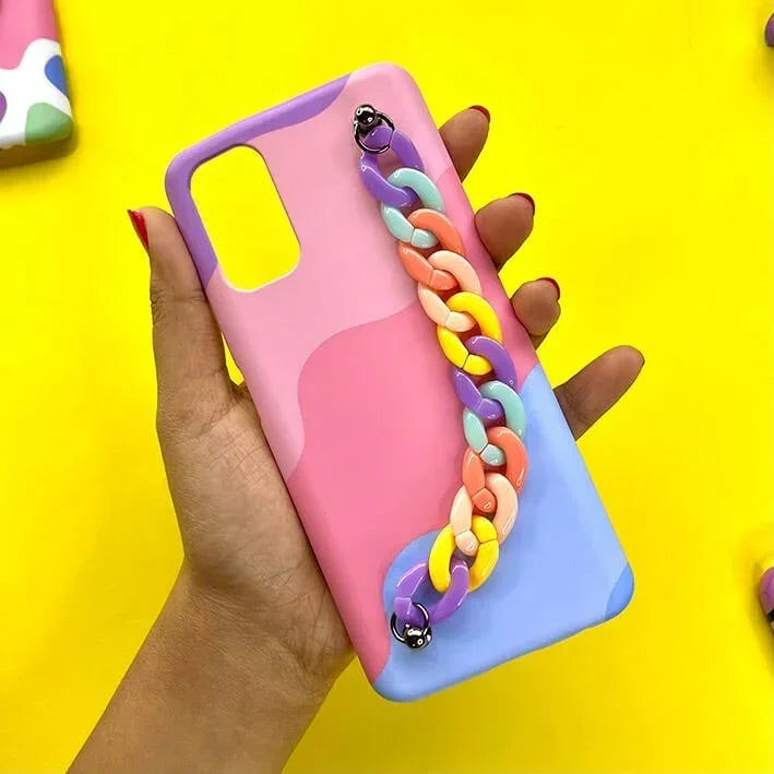 Hand holding pastel pink and blue phone case with colorful chain charm on yellow background