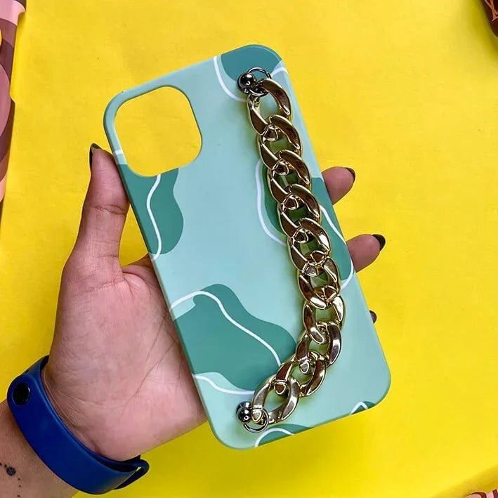 Green patterned phone case with gold chain grip, held in hand, on yellow background
