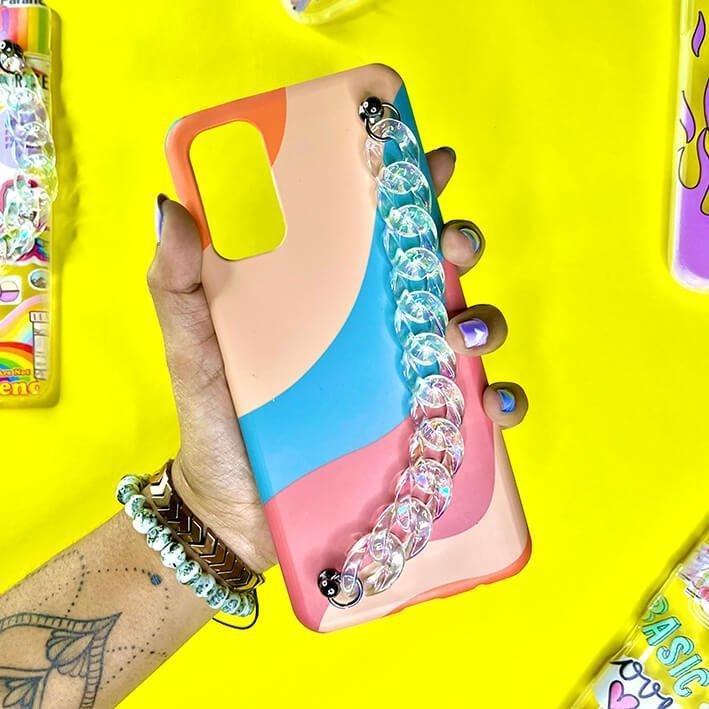 Colorful phone case with abstract pastel design and clear chain charm, held in hand on yellow background