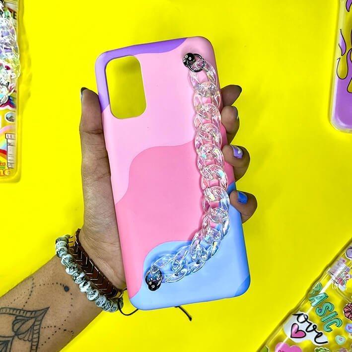 Pastel pink and blue phone case with clear chain charm, held in hand, on yellow background
