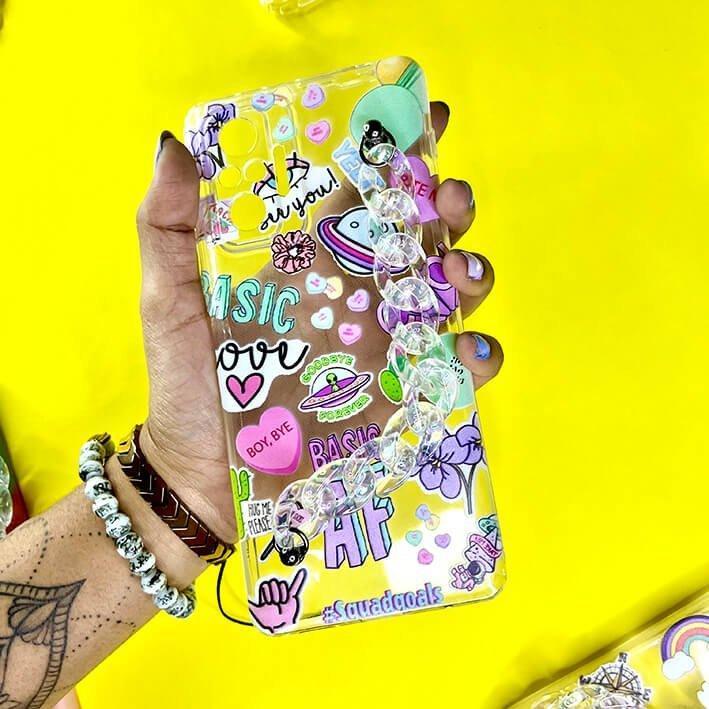 Colorful chain and charm phone case with stickers, held in hand on a yellow background