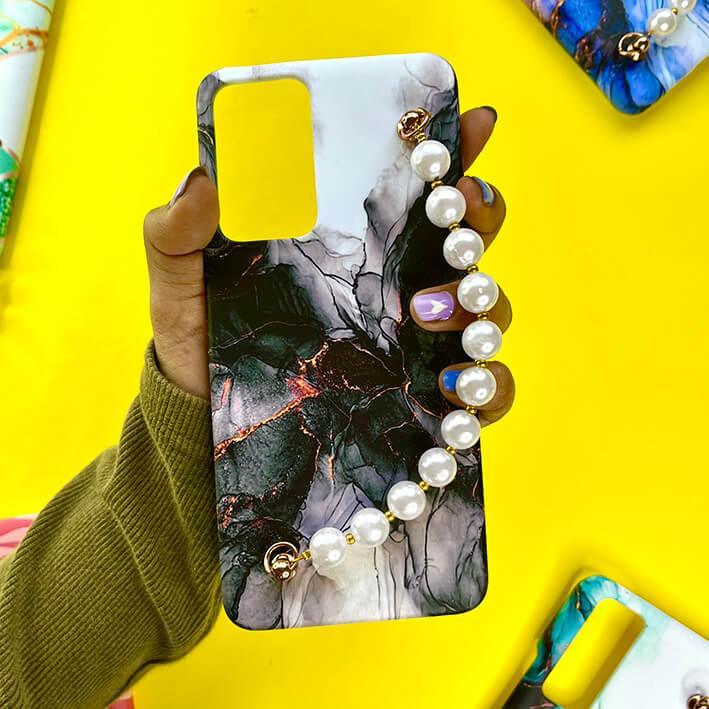 Black marble phone case with gold accents and pearl chain charm, held in hand on yellow background.