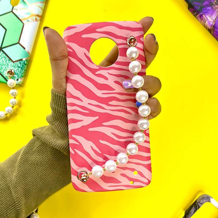 Pink zebra print phone case with pearl chain charm held in hand on yellow background