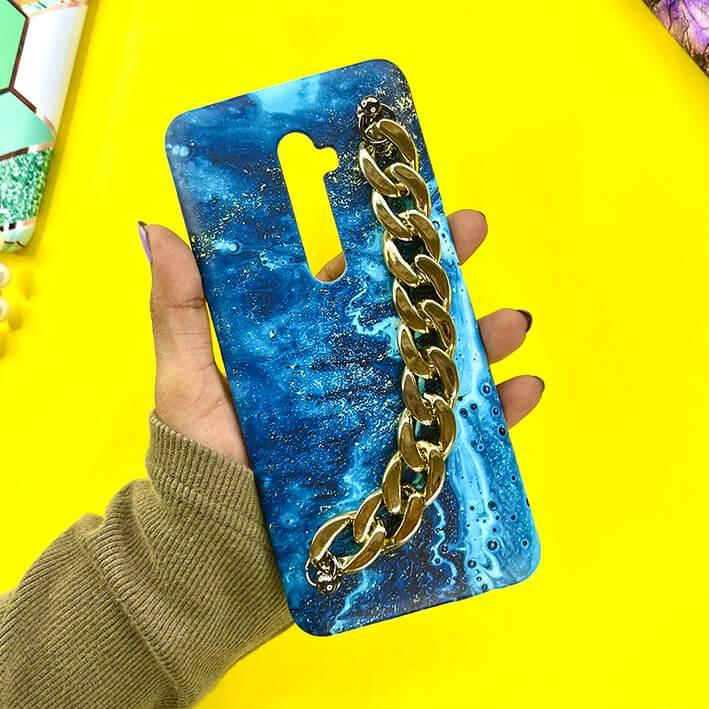 Blue marble phone case with gold chain charm, held in hand on yellow background