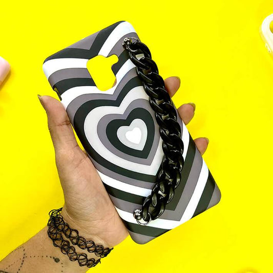 Black and white heart pattern phone case with black chain charm, held in hand on yellow background.