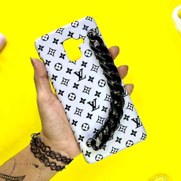 White mobile phone case with black monogram pattern and chunky black chain handle on yellow background