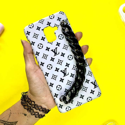 White mobile phone case with black monogram pattern and chunky black chain handle on yellow background