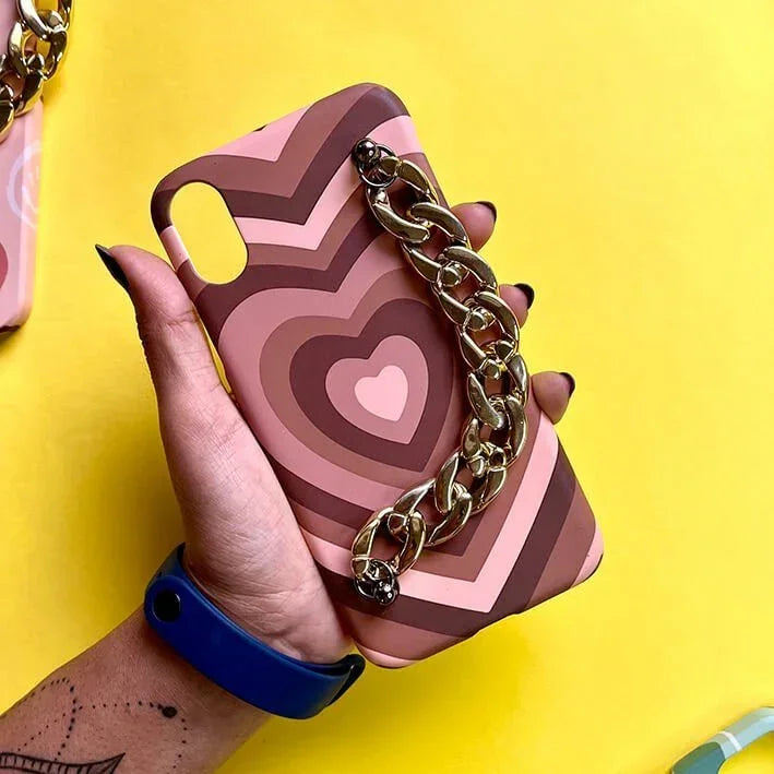 Pink and brown heart pattern phone case with gold chain grip, held against yellow background