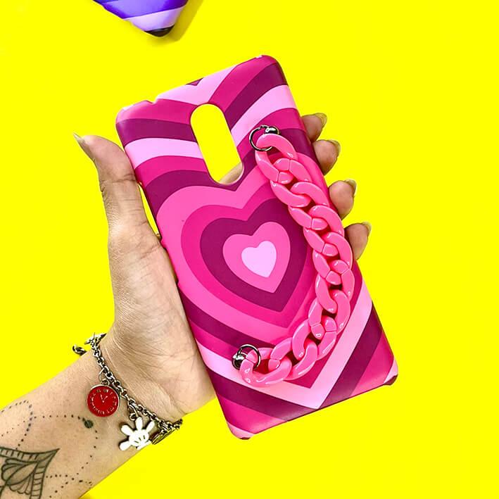 Pink heart pattern phone case with matching pink chain handle, held against yellow background