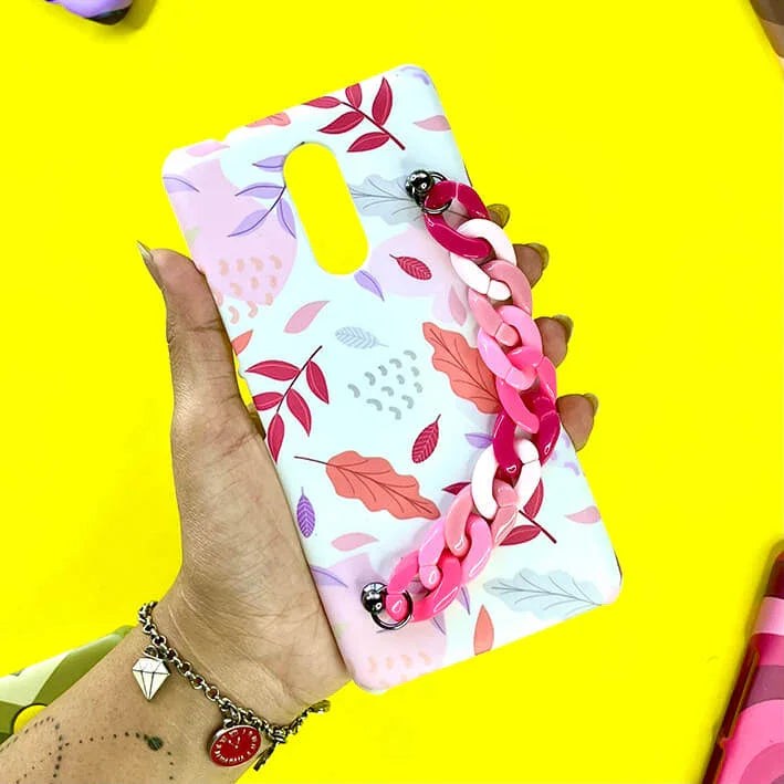 Floral leaf print phone case with pink chain strap, held in hand on yellow background.