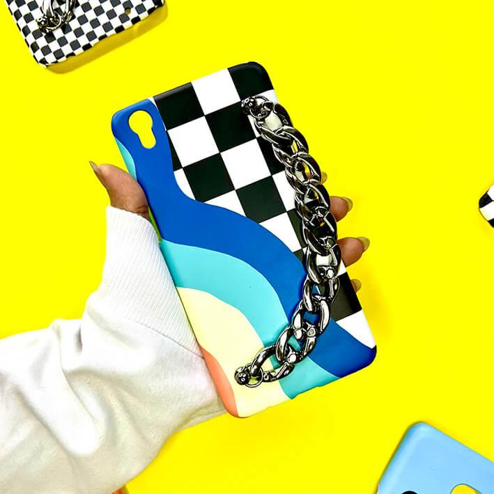 Hand holding a checkered and rainbow wavy phone case with a silver chain on yellow background