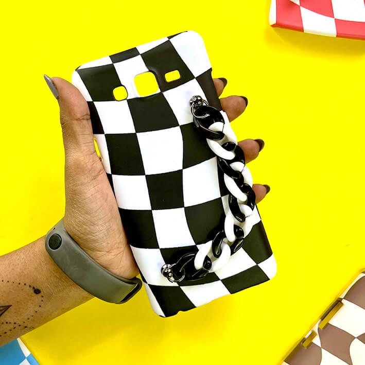 Black and white checkered phone case with matching chain handle, held over yellow background