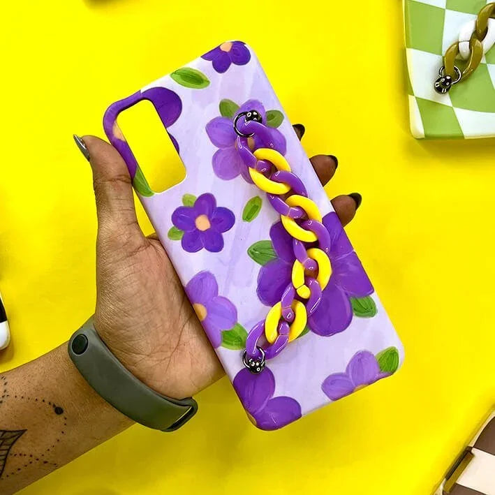 Purple floral phone case with yellow and purple chain charm, held against a yellow background