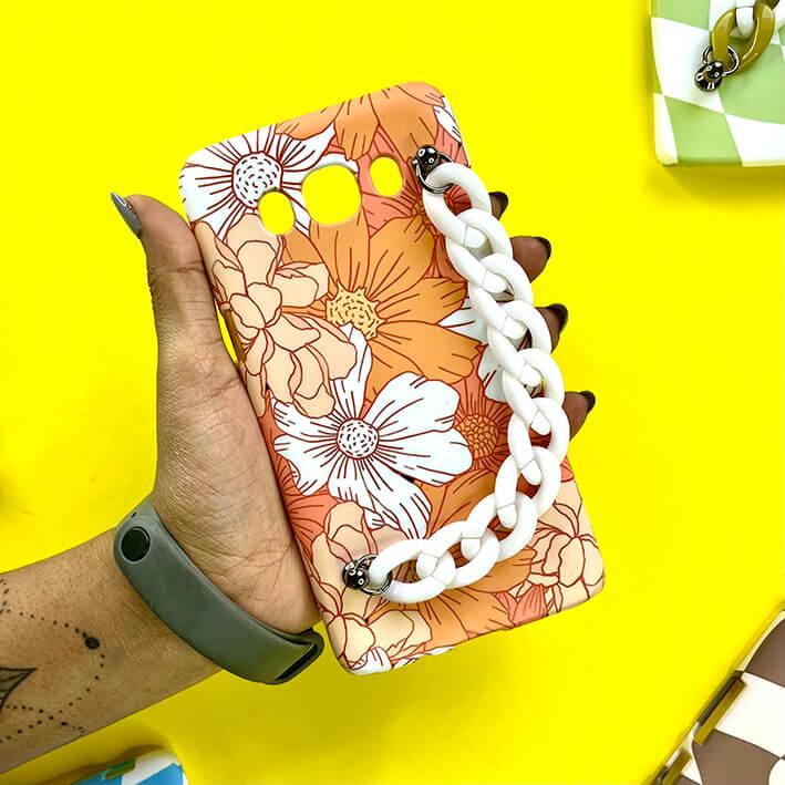 Floral phone case with white chain charm held in hand on bright yellow background