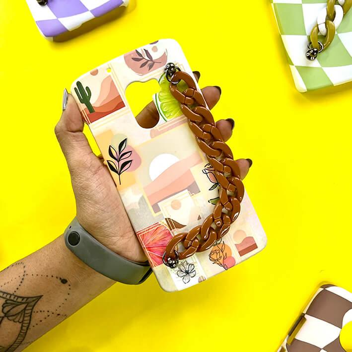 Hand holding abstract art phone case with brown chain grip on yellow background