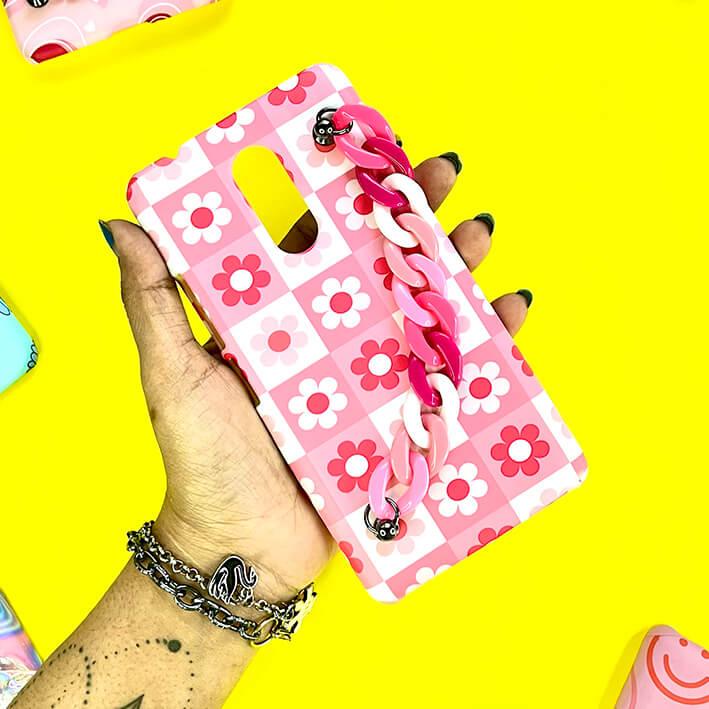 Pink floral checkerboard phone case with pink chain charm held in hand on yellow background