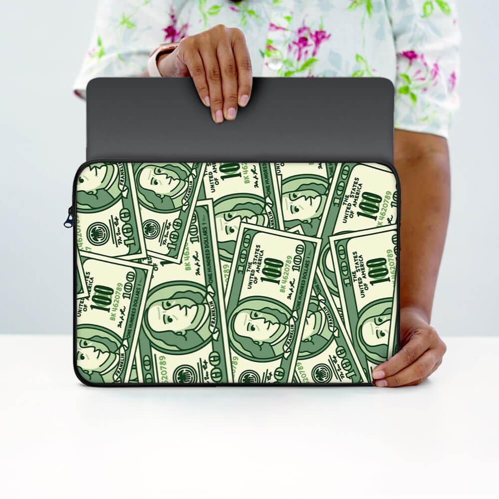 Person holding laptop sleeve with money print design, cartoon cash pattern, 13-inch size.