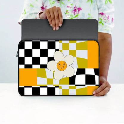 Person holding a 13-inch laptop sleeve with black, white, and yellow checkered pattern and a smiling flower design.