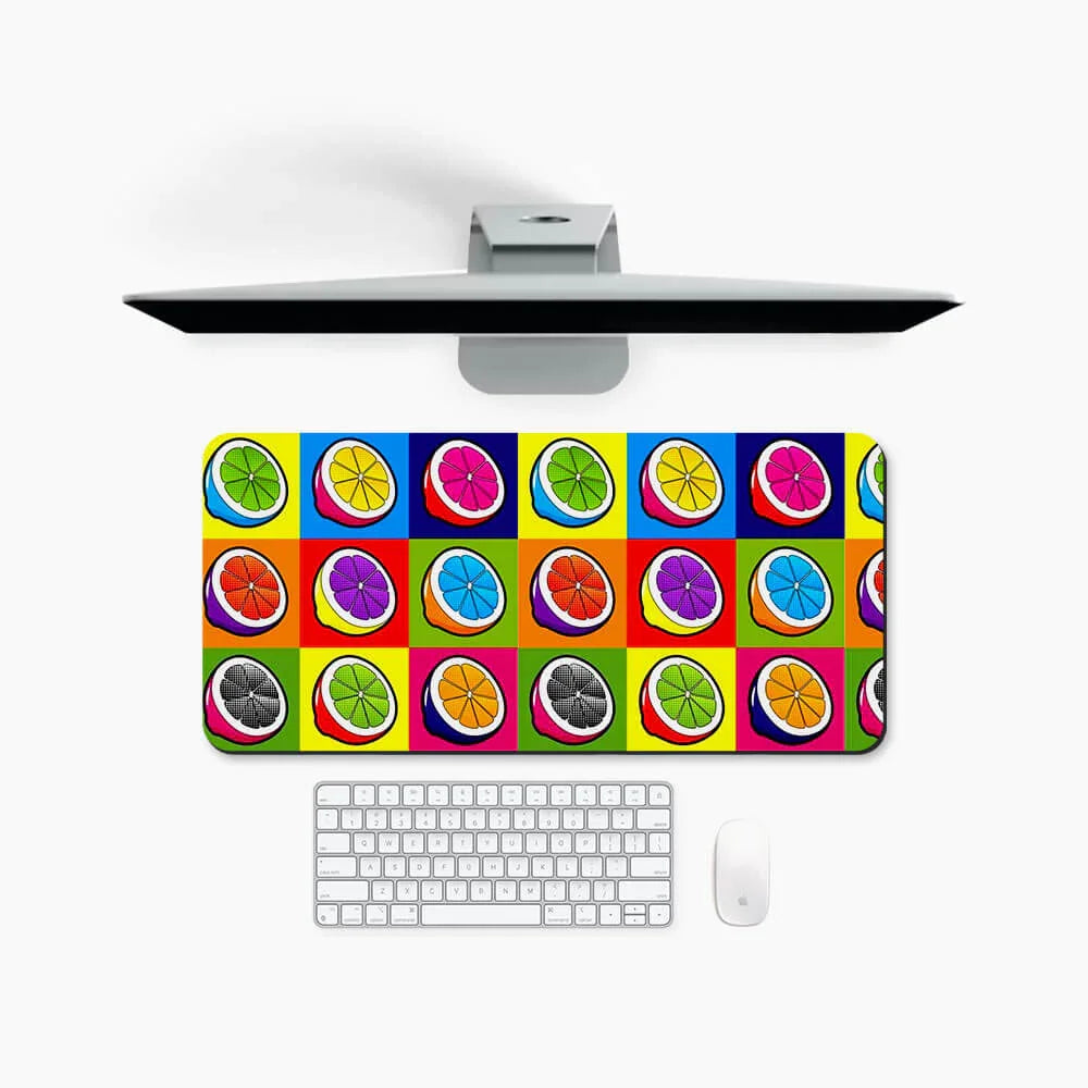 Colorful desk mat with citrus fruit pop art design, shown with monitor, keyboard, and mouse.
