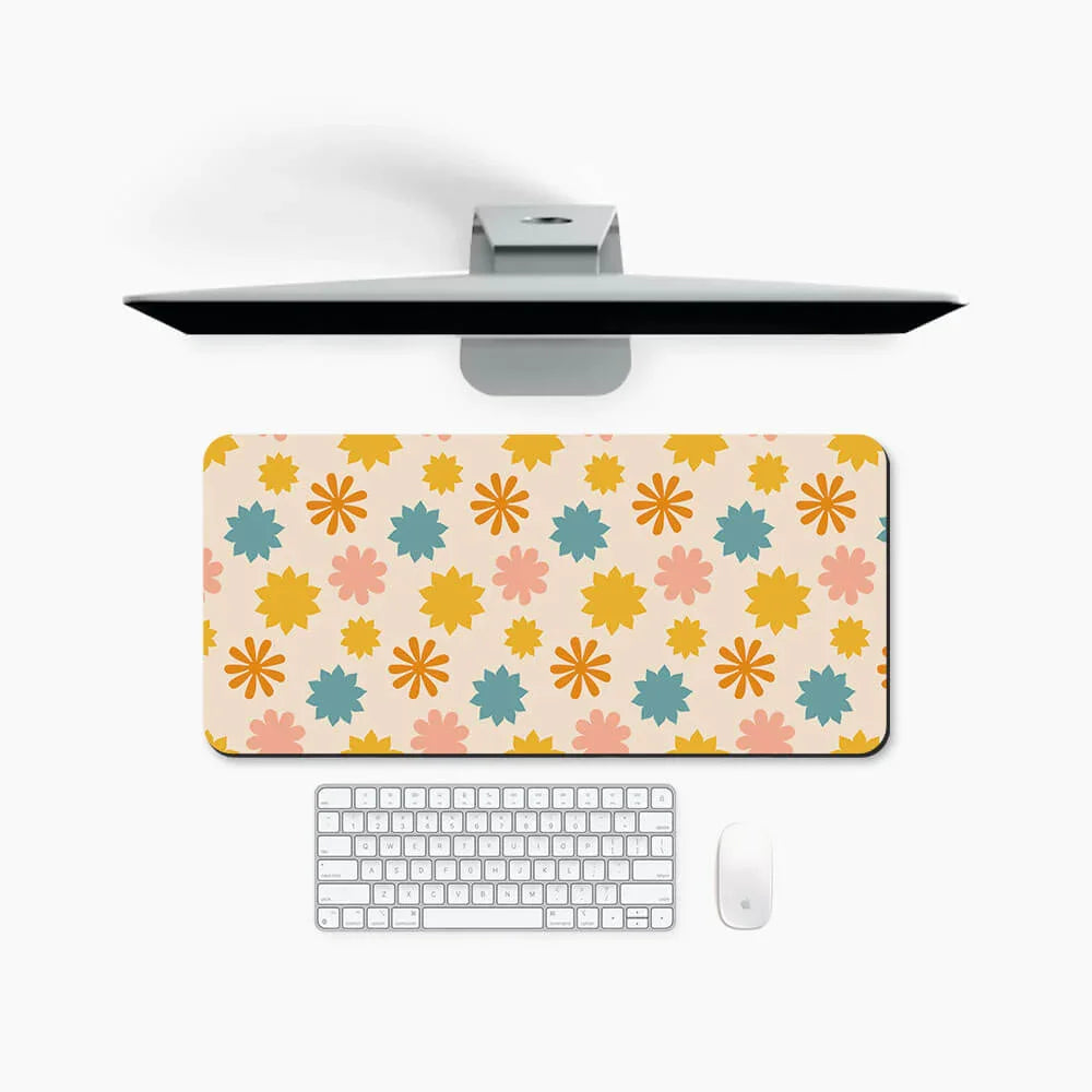 Floral desk mat with yellow, blue, and pink pattern on white desktop with keyboard, mouse, and monitor.