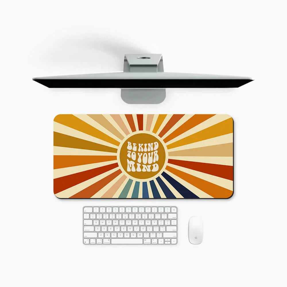 Colorful desk mat with 'Be Kind to Your Mind' text, sunburst retro design, on modern desk setup