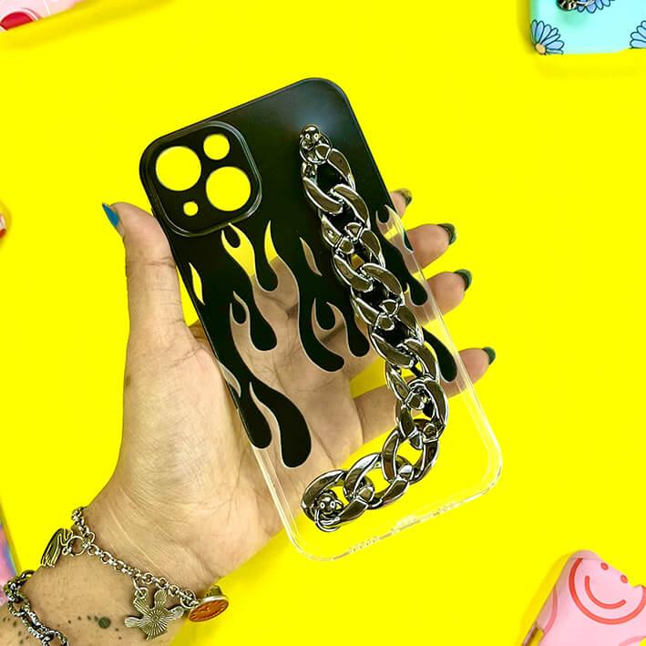 Clear phone case with black flame design and silver chain charm, held in hand on yellow background