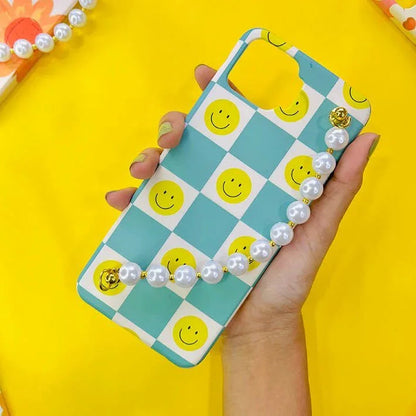 Checkerboard phone case with yellow smiley faces and pearl charm chain, held in hand