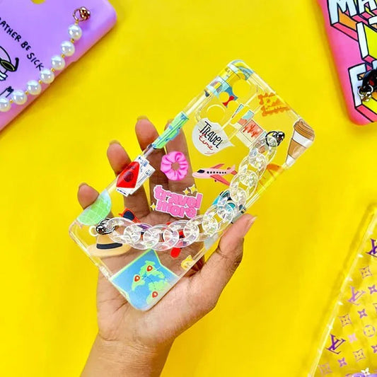 Clear travel-themed phone case with charms and chain handle, held on yellow background