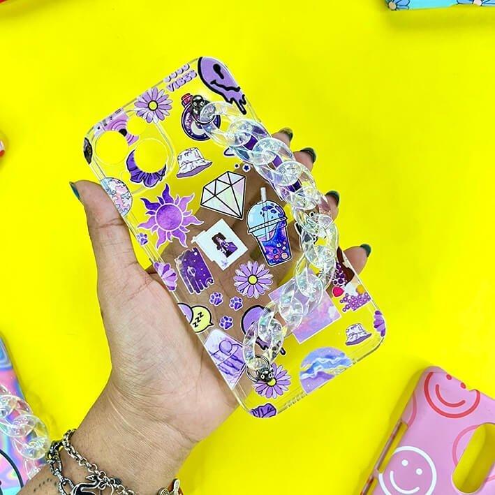 Transparent phone case with purple and violet stickers and a chunky chain, held in hand