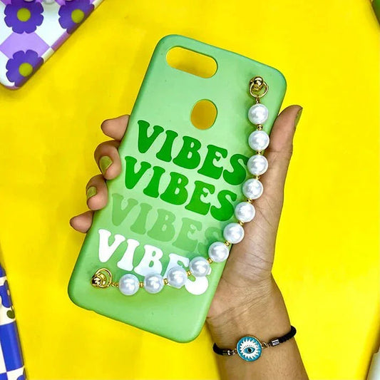 Green phone case with 'VIBES' text and pearl chain charm, held in hand, on yellow background