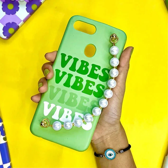Green phone case with 'VIBES' text and pearl chain charm, held in hand, on yellow background