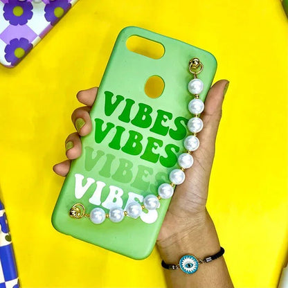 Green phone case with 'VIBES' text and pearl chain charm, held in hand, on yellow background