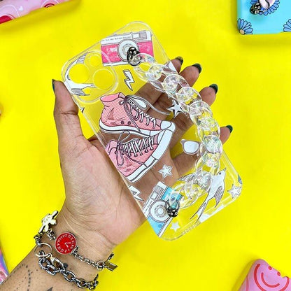 Clear phone case with pink sneakers, camera, and charm chain, held against yellow background