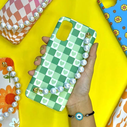 Green checkered phone case with white heart pattern and pearl chain, held in hand on yellow background