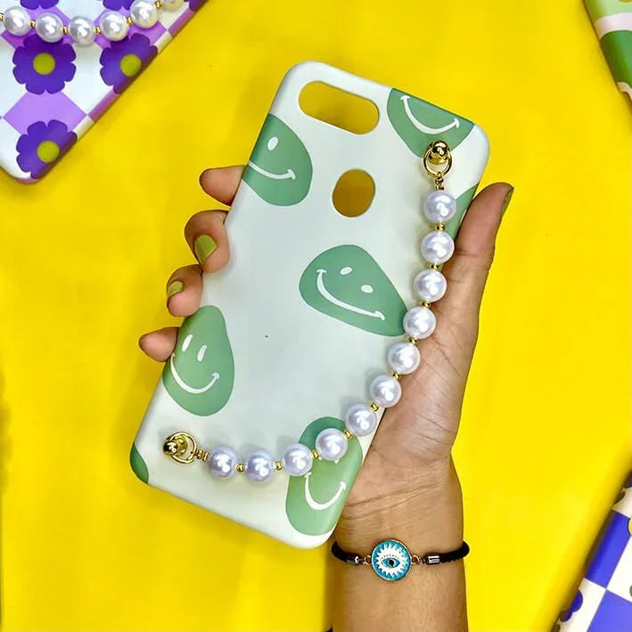 Green smiley face phone case with pearl chain charm, held in hand on yellow background