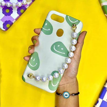 Green smiley face phone case with pearl chain charm, held in hand on yellow background