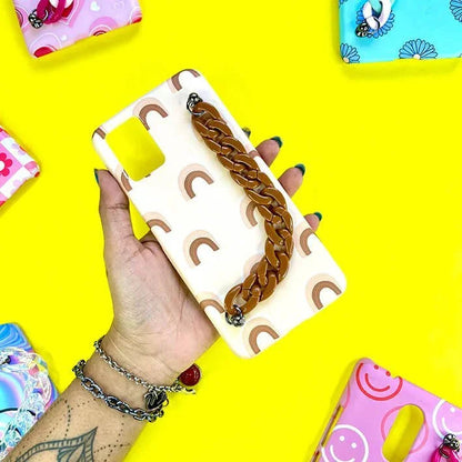 Cream phone case with rainbow print and brown chain handle, held on yellow background