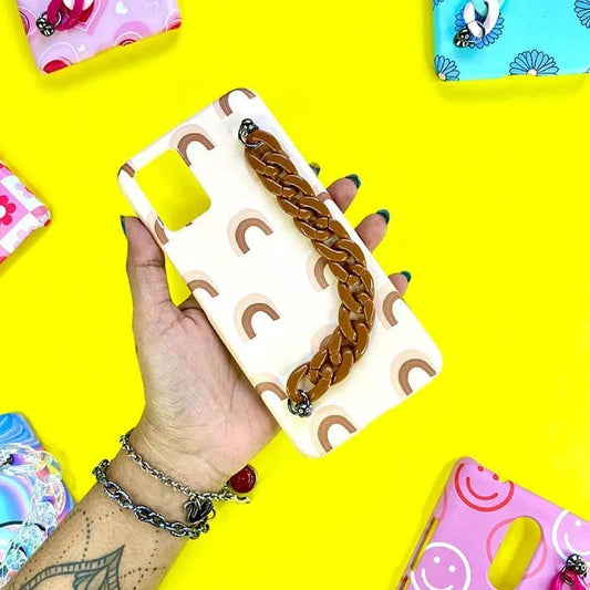 Cream phone case with rainbow print and brown chain handle, held on yellow background