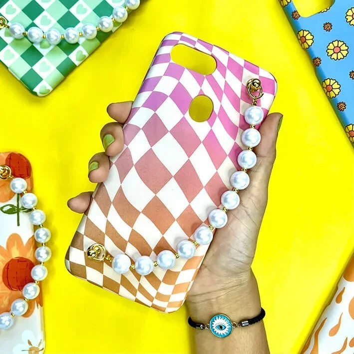 Pink and white checkered phone case with pearl chain, held in hand, on yellow background