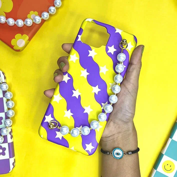 Yellow and purple star pattern phone case with pearl chain charm, held in hand on yellow background