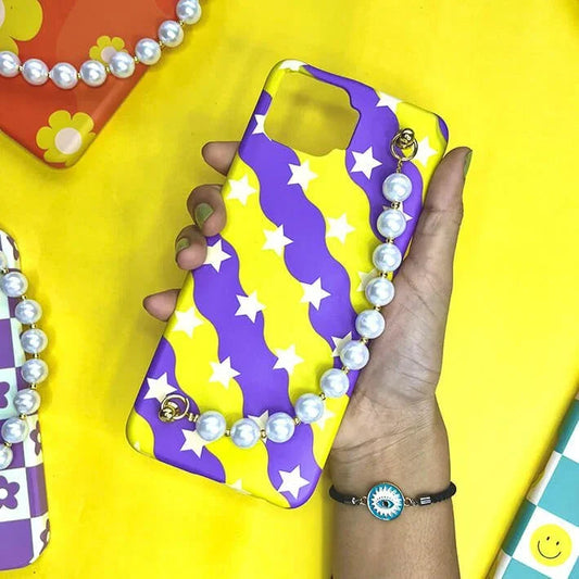 Yellow and purple star pattern phone case with pearl chain charm, held in hand on yellow background