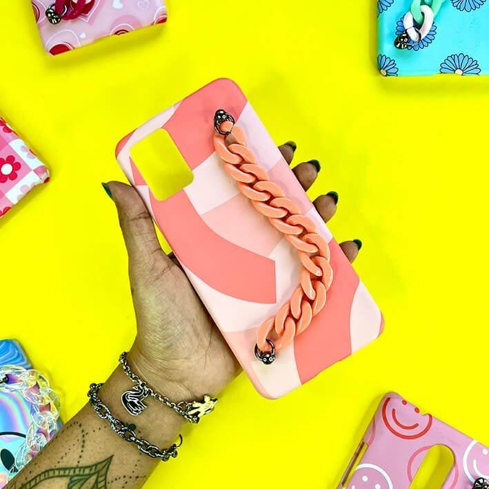 Pink and peach chain phone case with abstract design held in hand, colorful cases in background