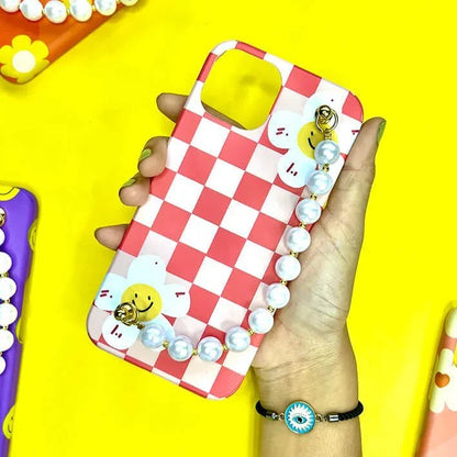 Red checkered phone case with smiley flowers and pearl chain charm, held in hand on yellow background