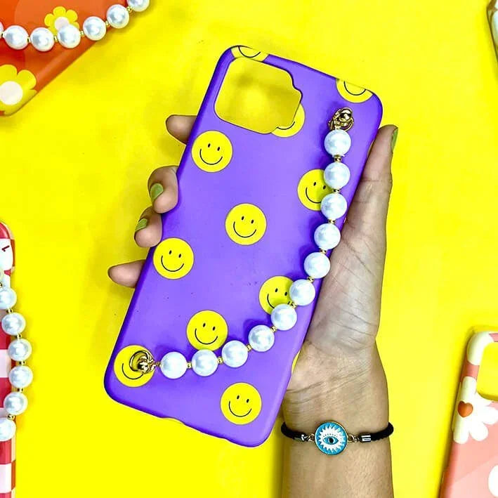 Purple phone case with yellow smiley faces and pearl chain held in hand on yellow background