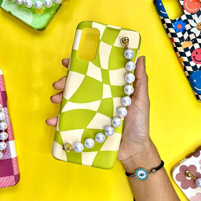 Hand holding a green and cream wavy checkered phone case with pearl chain charm on yellow background