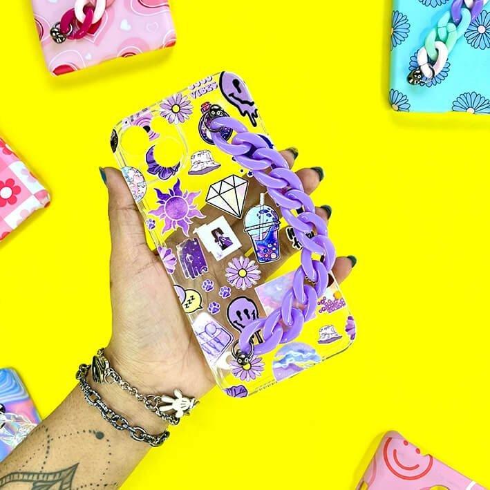 Hand holding a cute phone case with purple chain and cartoon charms on yellow background