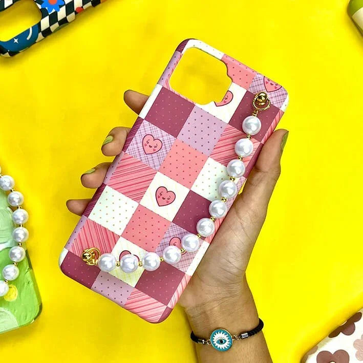 Hand holding pink patchwork phone case with heart pattern and pearl chain charm