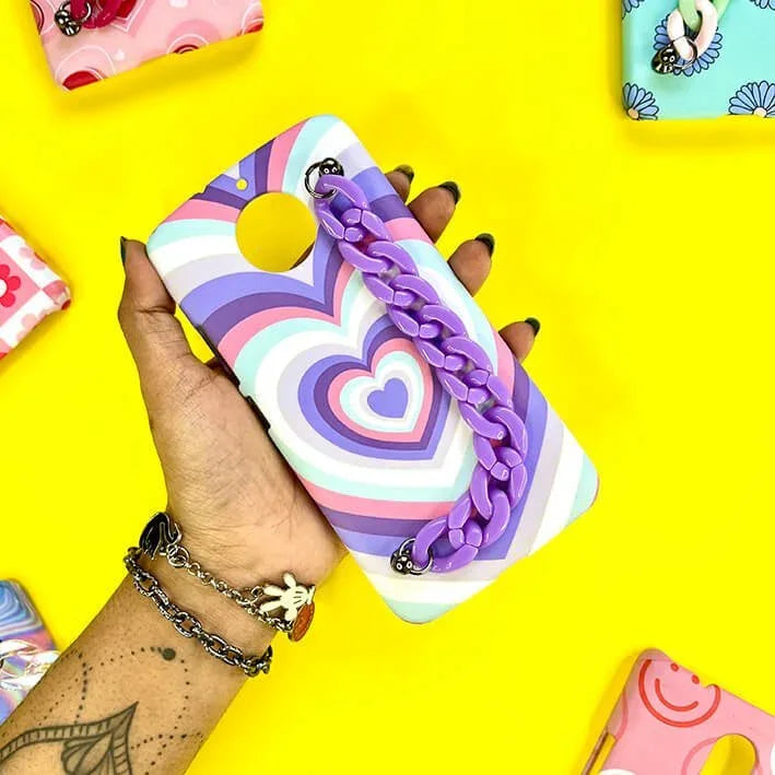 Hand holding a pastel heart pattern phone case with a purple chain charm, vibrant yellow background