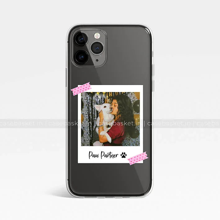 Black transparent phone case with a polaroid design showing a woman hugging a white dog, text 'Paw Partner'.